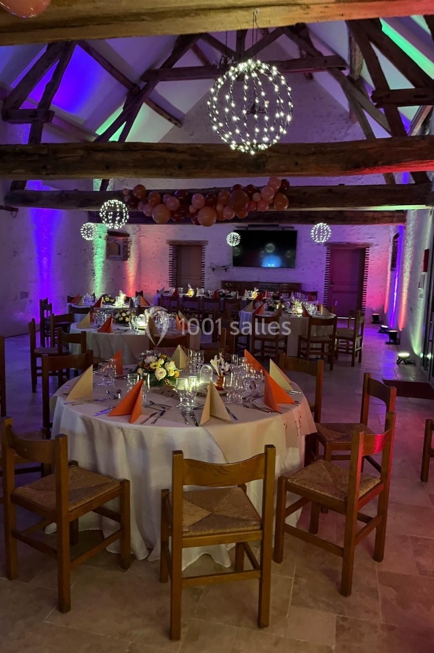 Salle de réception décorée avec des tables dressées, éclairage coloré et guirlandes lumineuses suspendues.