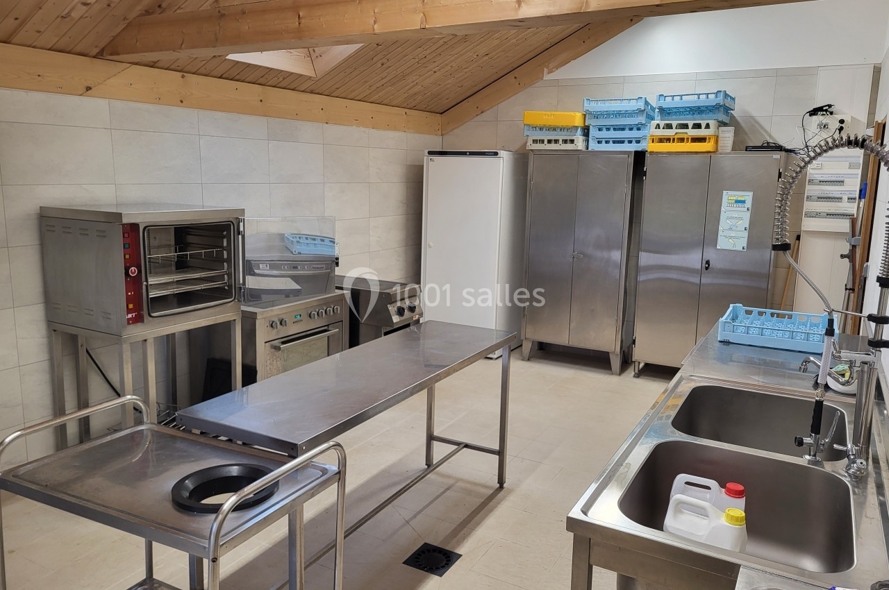 Cuisine professionnelle avec équipements en inox, comprenant un four, des éviers, des armoires et des bacs de rangement.