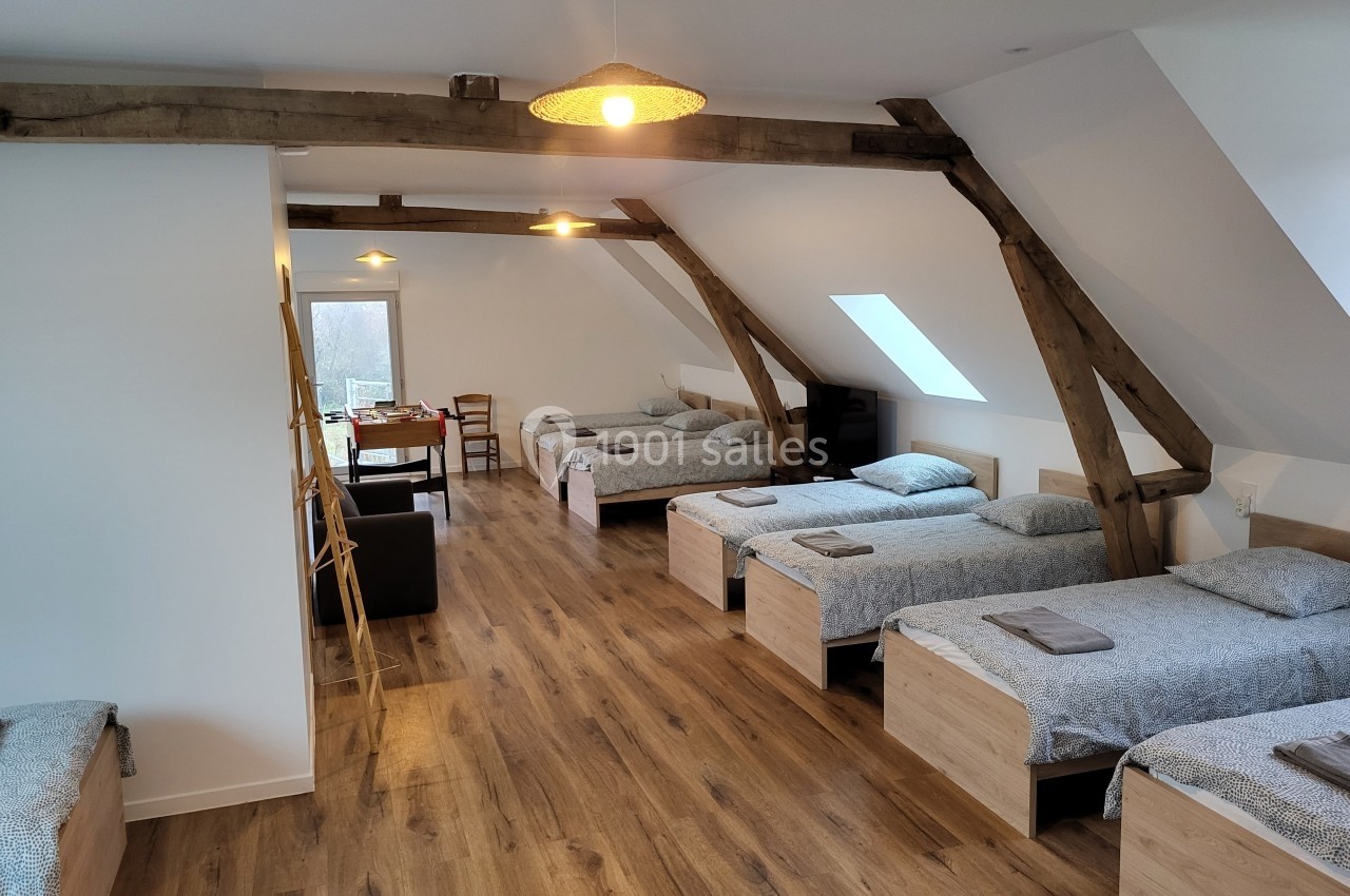 Dortoir lumineux avec poutres apparentes, six lits simples, parquet en bois et table au fond de la pièce.