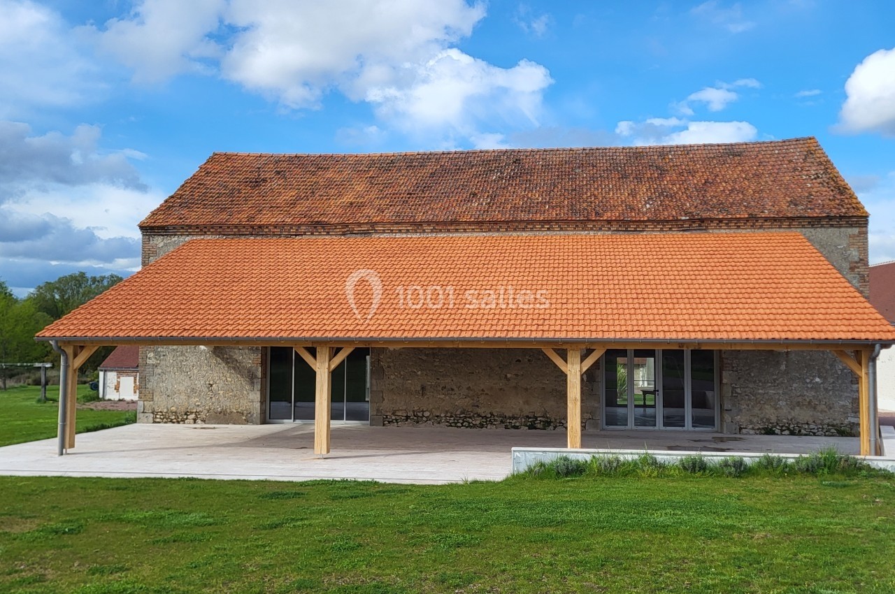 Bâtiment en pierre rénové avec une toiture en tuiles rouges et une avancée couverte soutenue par des poteaux en bois.
