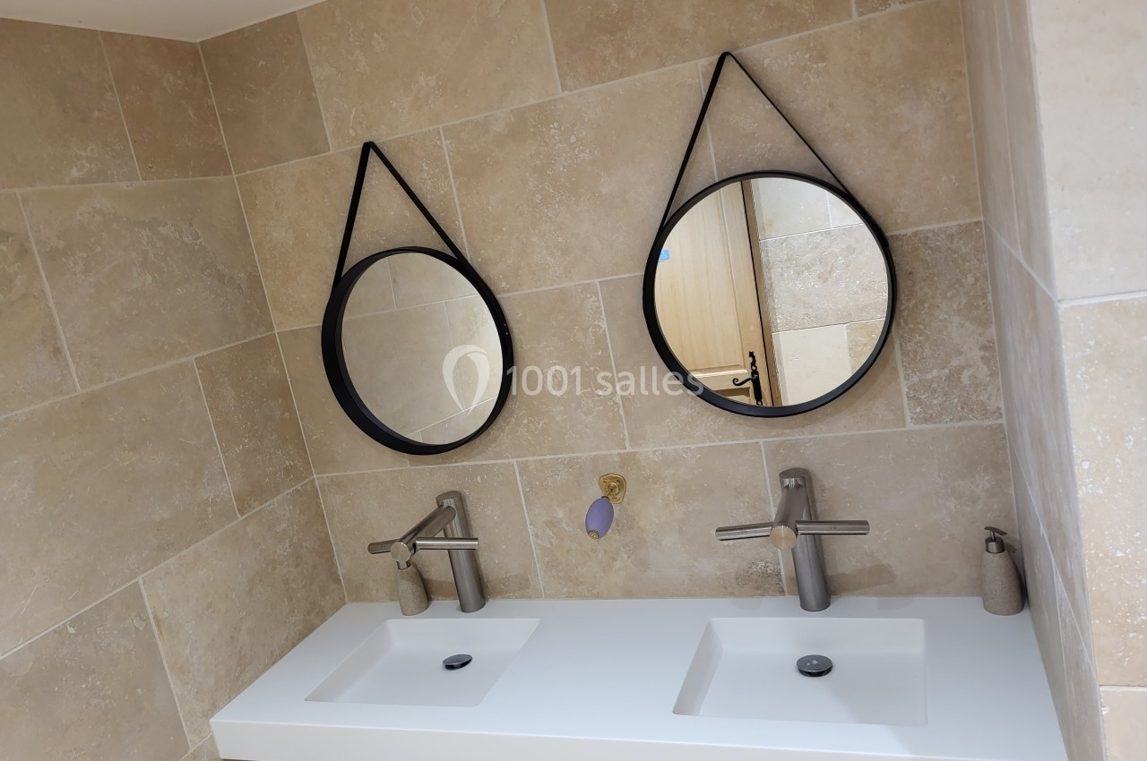 Deux lavabos blancs avec robinets modernes, miroirs ronds suspendus et murs en carrelage beige.
