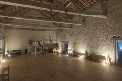 Bâtiment en pierre éclairé par des lumières extérieures, dans une cour sombre au crépuscule.
