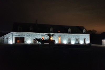Bâtiment en pierre éclairé par des lumières extérieures, dans une cour sombre au crépuscule.