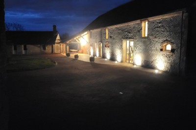 Bâtiment en pierre éclairé par des lumières extérieures, dans une cour sombre au crépuscule.