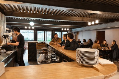 Miniature Location salle Ivry-sur-Seine (Val-de-Marne) - Ivrywood #37 Salle de réunion avec une grande table en bois, chaises en cuir marron, fenêtres et kitchenette en arrière-plan.