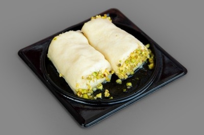 Deux pâtisseries roulées garnies de pistaches hachées, présentées sur une assiette noire.