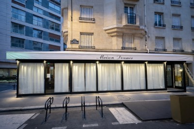 Bar avec comptoir en marbre, tabourets en velours orange et étagères éclairées exposant des bouteilles d'alcool.