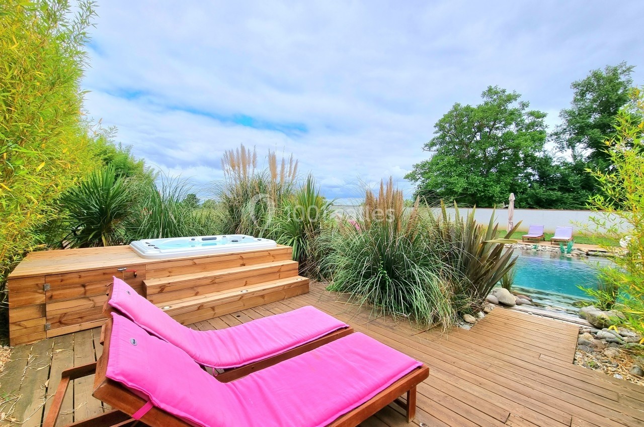 Terrasse en bois avec deux transats roses, un jacuzzi et une piscine entourée de végétation.
