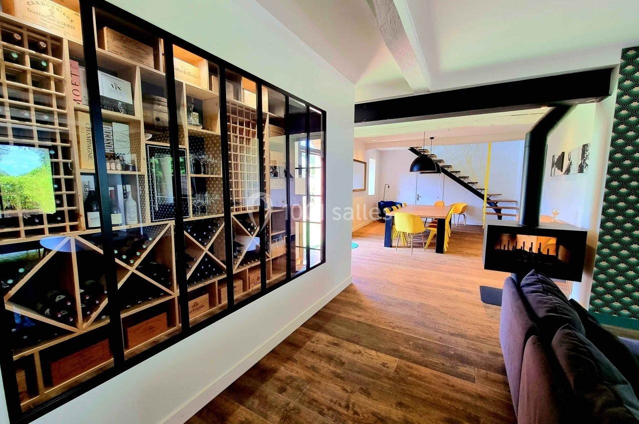 Vue intérieure d'une maison avec une cave à vin vitrée, un salon, une cheminée moderne et une salle à manger lumineuse.