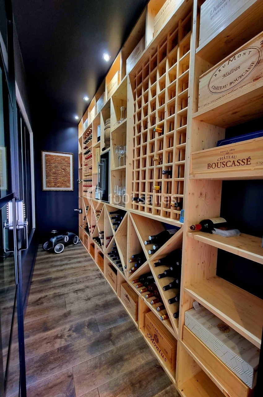 Cave à vin moderne avec étagères en bois contenant des bouteilles, caisses et accessoires, éclairée par des spots.