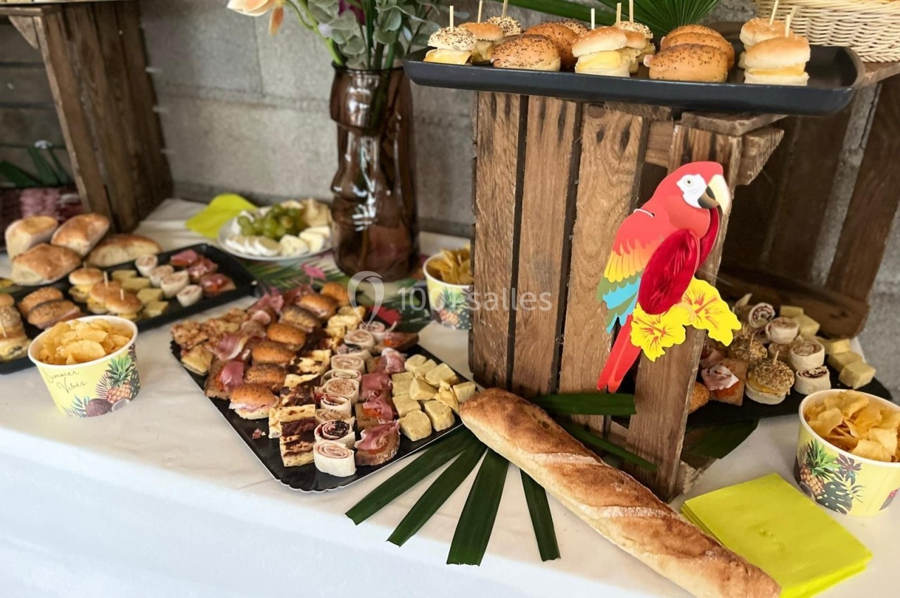 Buffet coloré avec assortiments de bouchées salées, pain, chips et décor tropical incluant un perroquet en papier.