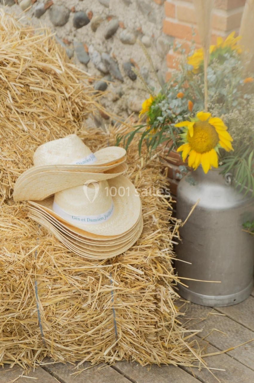 Deux chapeaux de paille posés sur une botte de foin, avec un tournesol et un bidon en métal en arrière-plan.