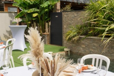 Table décorée avec des pampas et des nappes beige, installée dans un jardin avec des plantes tropicales en arrière-plan.