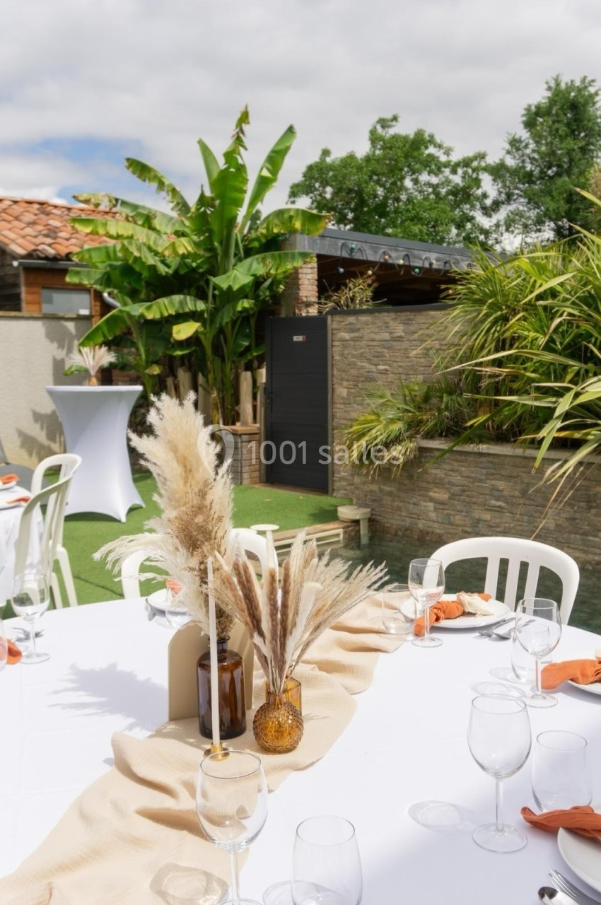 Table décorée avec des pampas et des nappes beige, installée dans un jardin avec des plantes tropicales en arrière-plan.