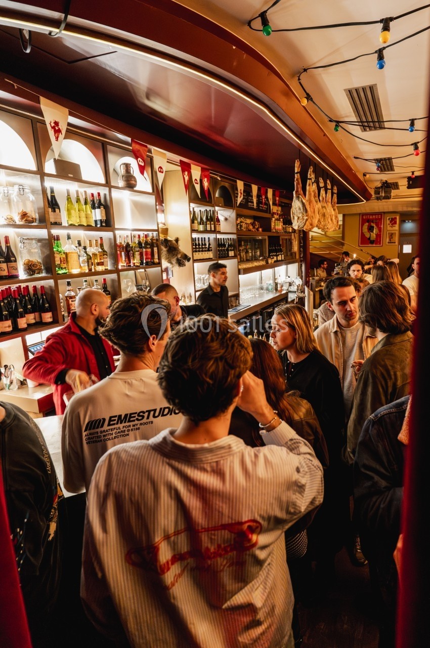 Des personnes discutent et se rassemblent dans un bar animé, entourées de bouteilles et de décorations chaleureuses.