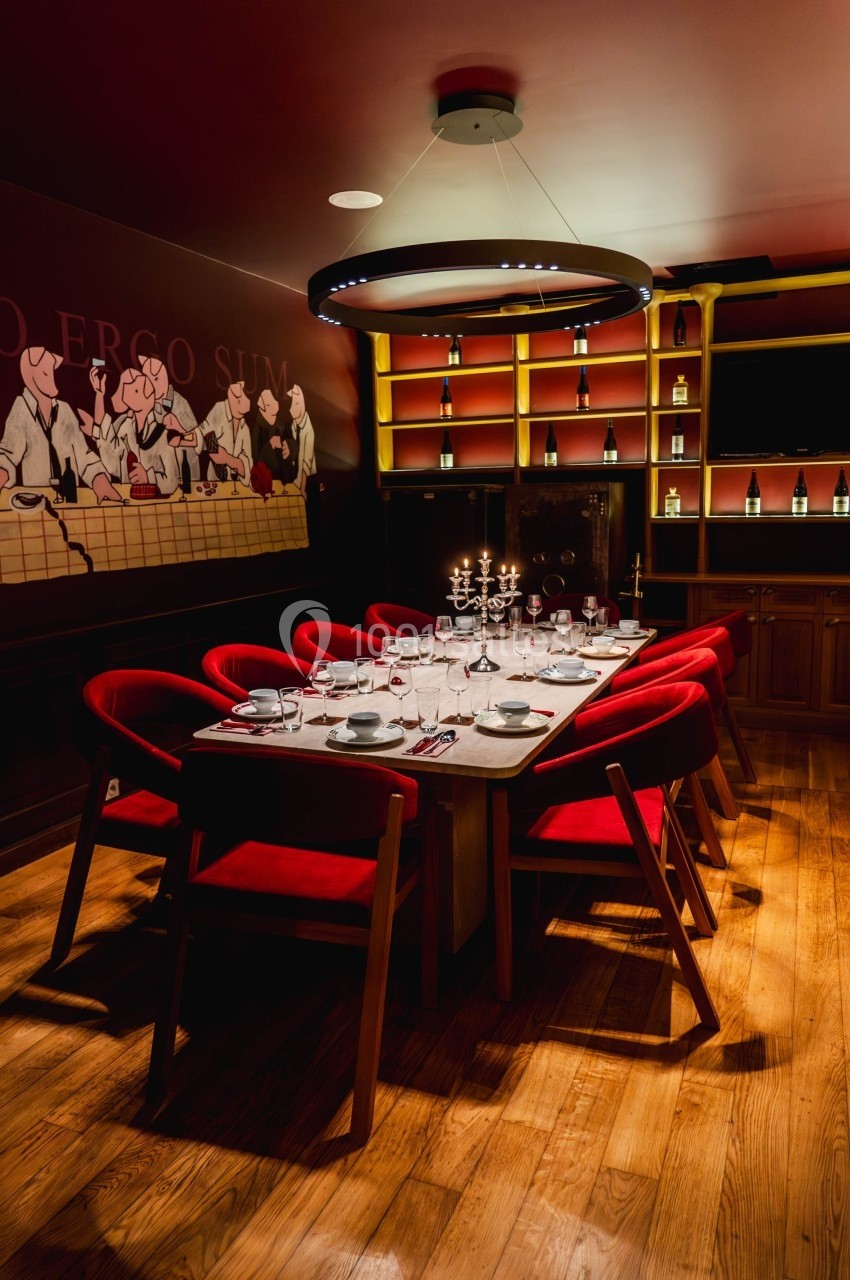 Salle à manger élégante avec table dressée, chaises rouges, bougeoirs allumés et étagères éclairées en arrière-plan.