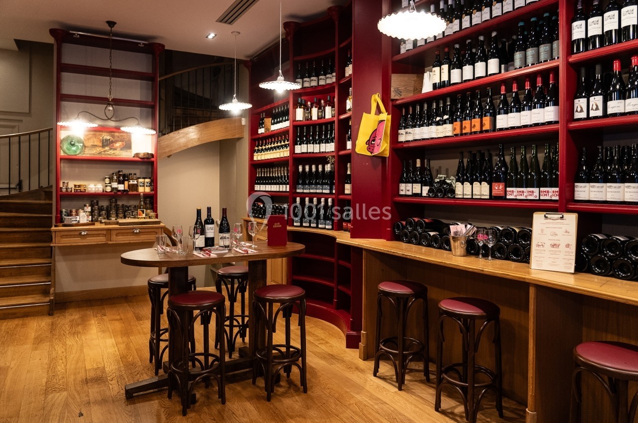 Salle chaleureuse avec étagères remplies de bouteilles de vin, table ronde en bois et tabourets dans un décor rustique.
