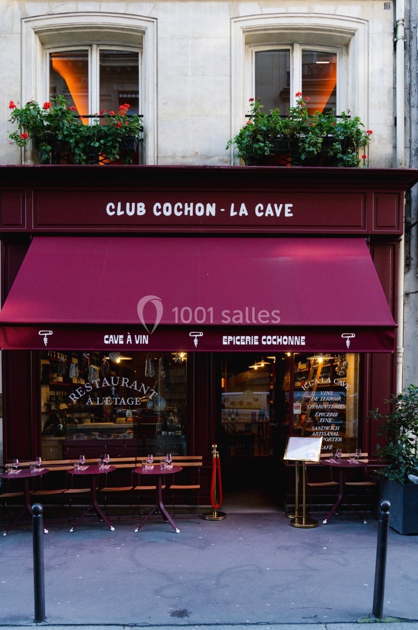Façade d'un restaurant avec terrasse, auvent rouge et inscriptions ’Club Cochon - La Cave’ et ’Épicerie Cochonne’.