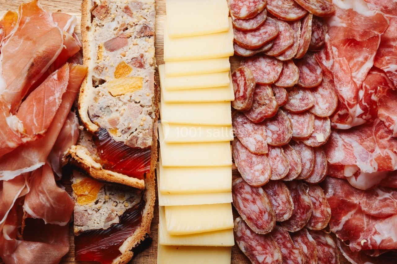Plateau composé de jambon cru, pâté en croûte, tranches de fromage et saucisson sec disposés sur une planche.