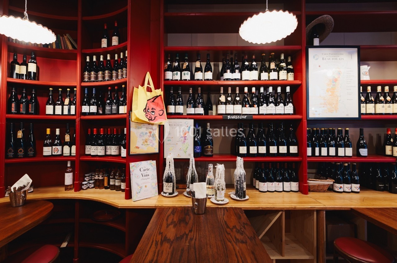 Étagères rouges remplies de bouteilles de vin, avec une carte et des affiches exposées sur un comptoir en bois.