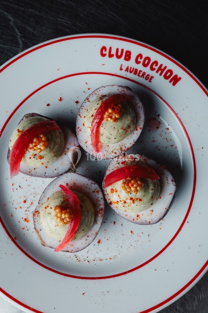 Quatre œufs mimosa garnis de crème, moutarde en grains et lamelles de pickles, présentés sur une assiette blanche.