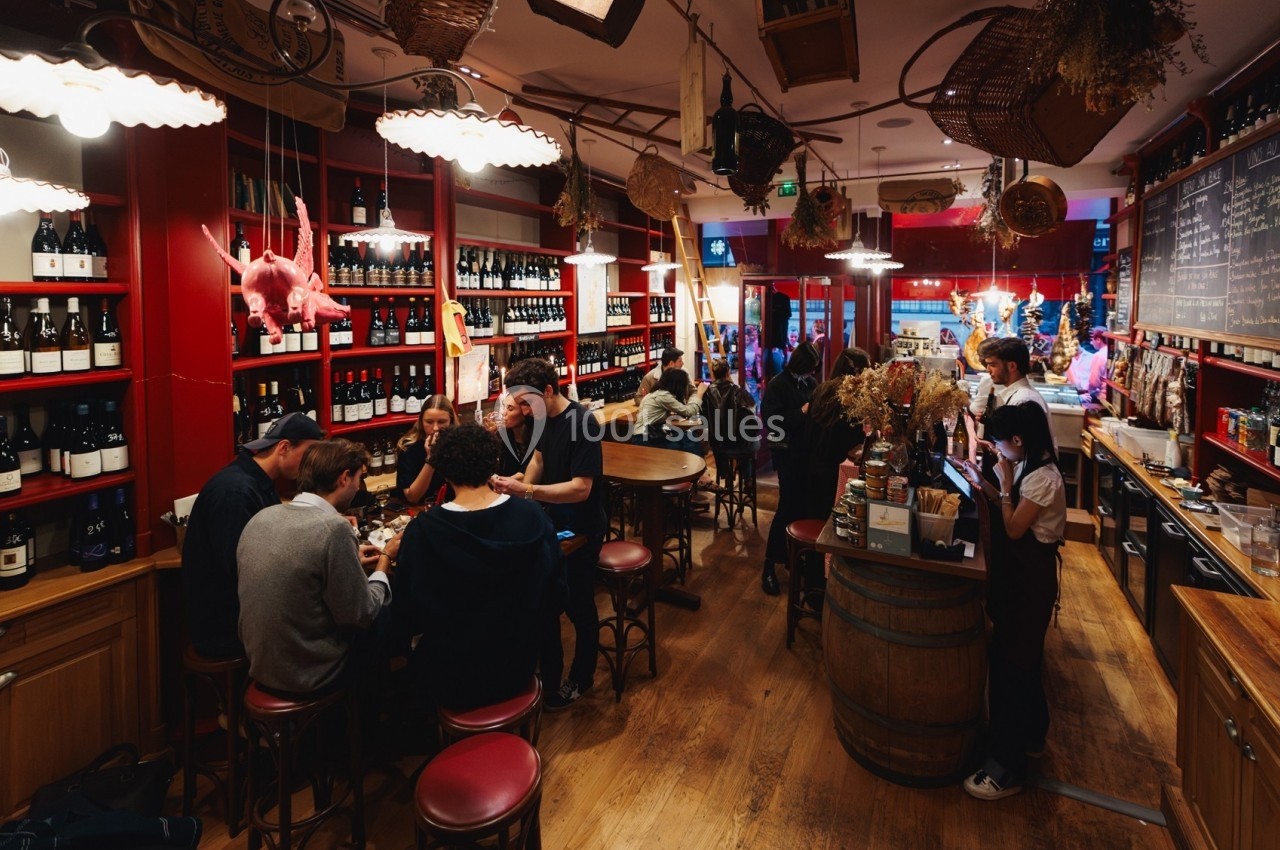 Intérieur d'un bar à vin animé avec des clients attablés, des étagères remplies de bouteilles et une ambiance chaleureuse.