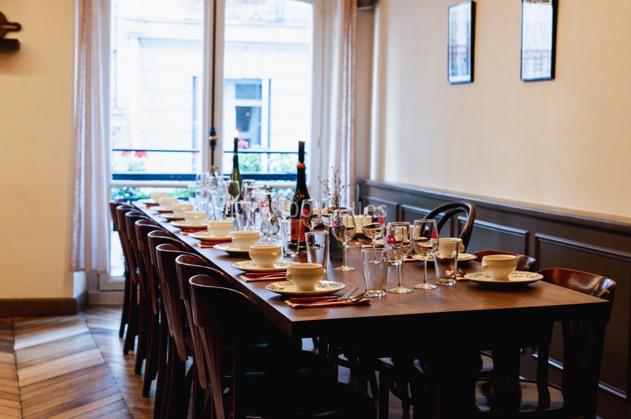 Table dressée avec vaisselle, verres et bouteilles de vin dans une salle lumineuse avec parquet et fenêtres donnant sur l…