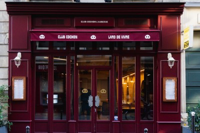 Façade d'un restaurant avec une enseigne ’Club Cochon - La Cave’, terrasse avec tables et chaises devant.