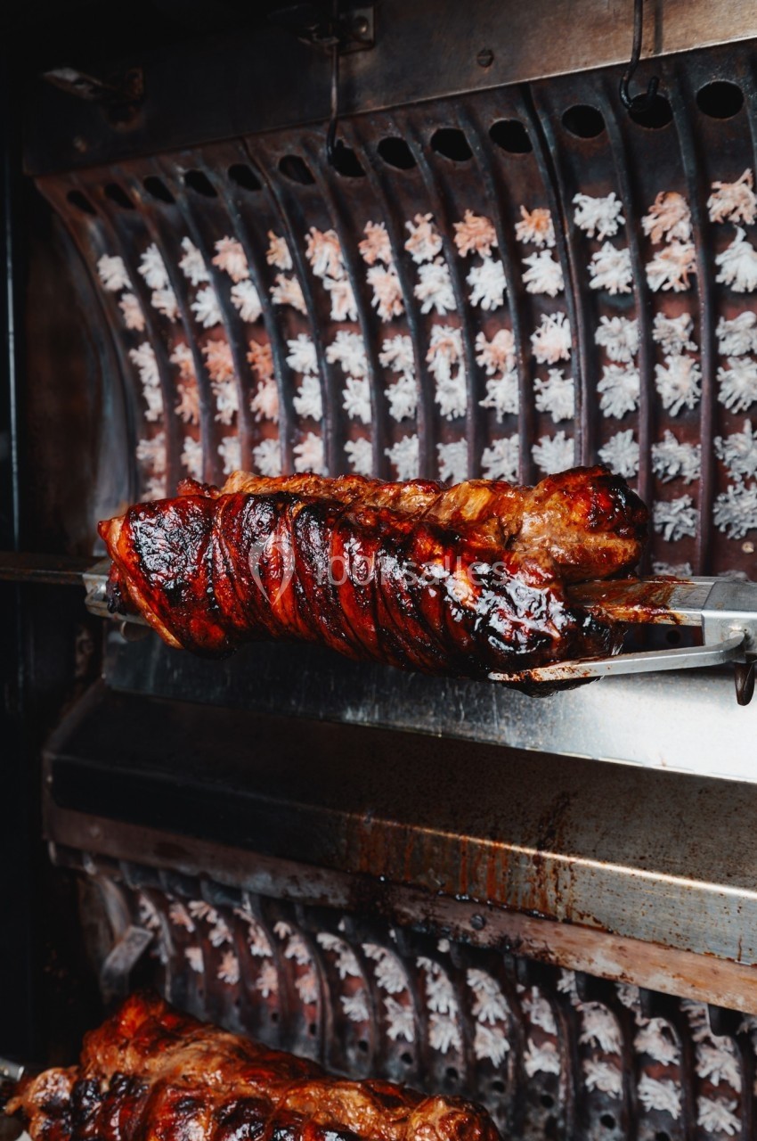 Viande rôtie sur une broche tournante dans un four, avec une surface dorée et caramélisée.