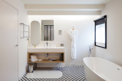 Salle de bain moderne avec baignoire, lavabo, miroir, peignoir suspendu et sol en damier noir et blanc.