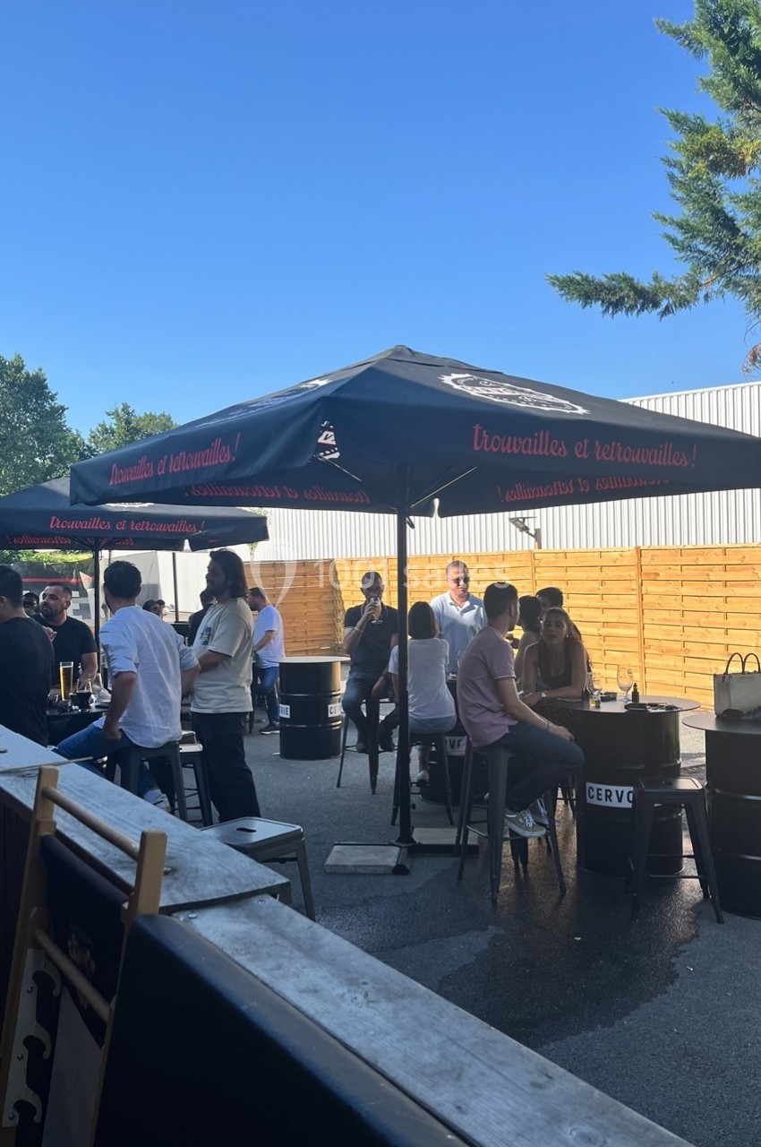 Des personnes discutent et partagent un moment convivial sous des parasols dans une terrasse extérieure ensoleillée.