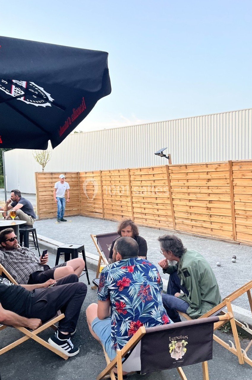 Groupe de personnes assises en extérieur sur des chaises, discutant près d'un terrain de pétanque et d'une clôture en bois.