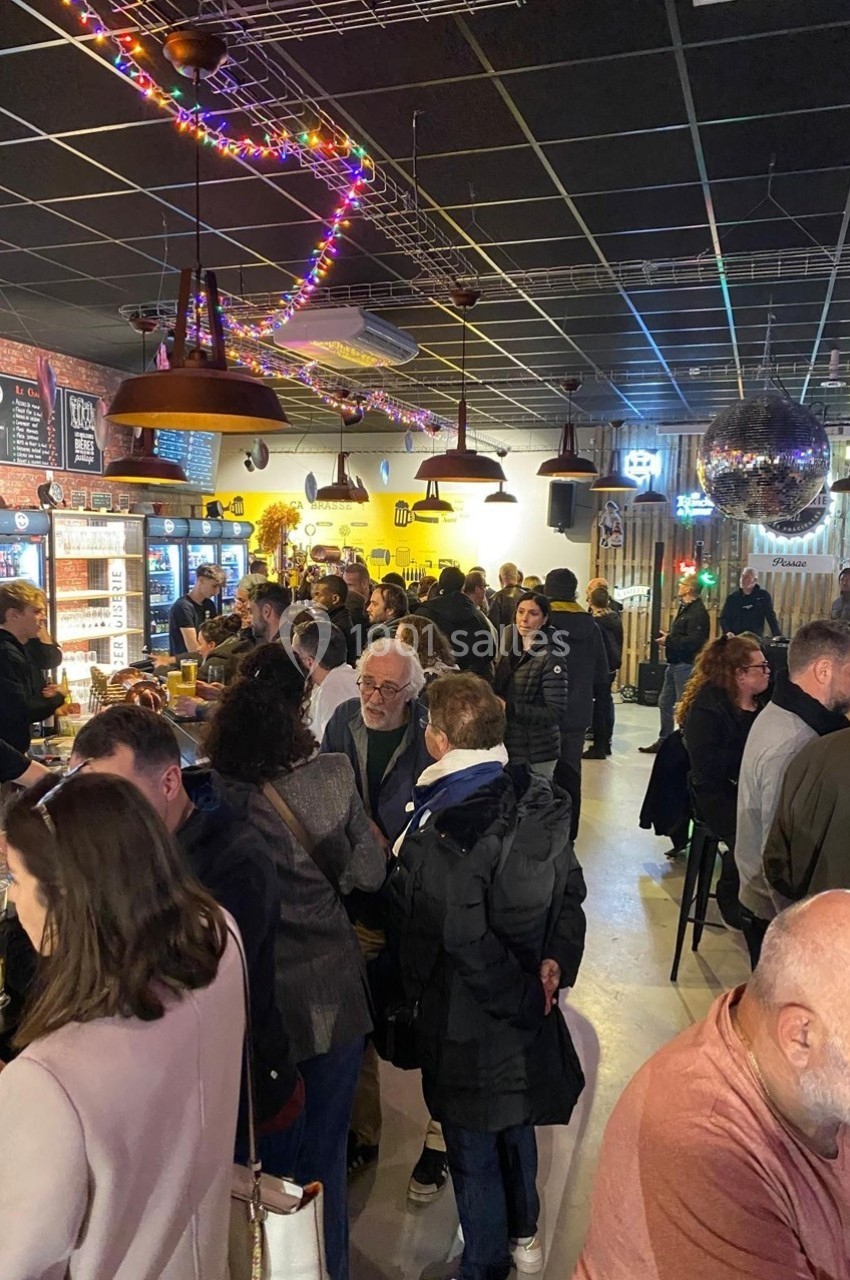 Des personnes discutent et se détendent dans un bar animé, avec des lumières colorées et un comptoir en arrière-plan.