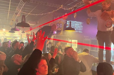 Des personnes dans un bar participent à une animation avec des lasers rouges, sous un éclairage tamisé.