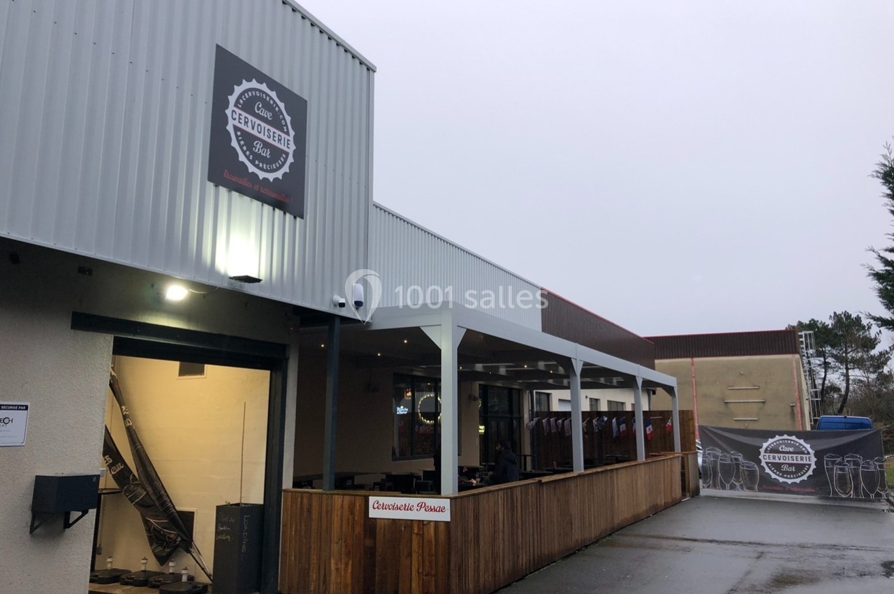 Façade d'une brasserie avec terrasse couverte en bois, éclairage extérieur et enseigne visible sous un ciel gris.