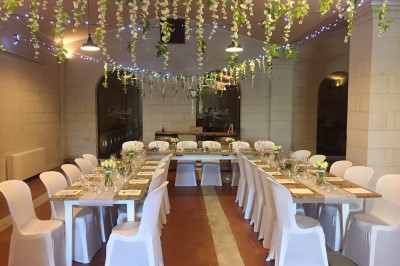 Table dressée avec vaisselle élégante, fleurs et bouteille, dans une salle avec des tonneaux en arrière-plan.