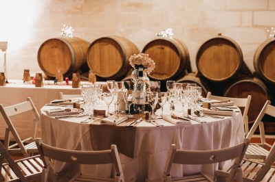 Table dressée avec vaisselle élégante, fleurs et bouteille, dans une salle avec des tonneaux en arrière-plan.