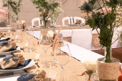 Un couple en tenue de mariage pose sous un arbre, entouré de chaises blanches et de décorations végétales en extérieur.