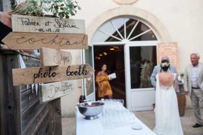 Un couple en tenue de mariage pose sous un arbre, entouré de chaises blanches et de décorations végétales en extérieur.