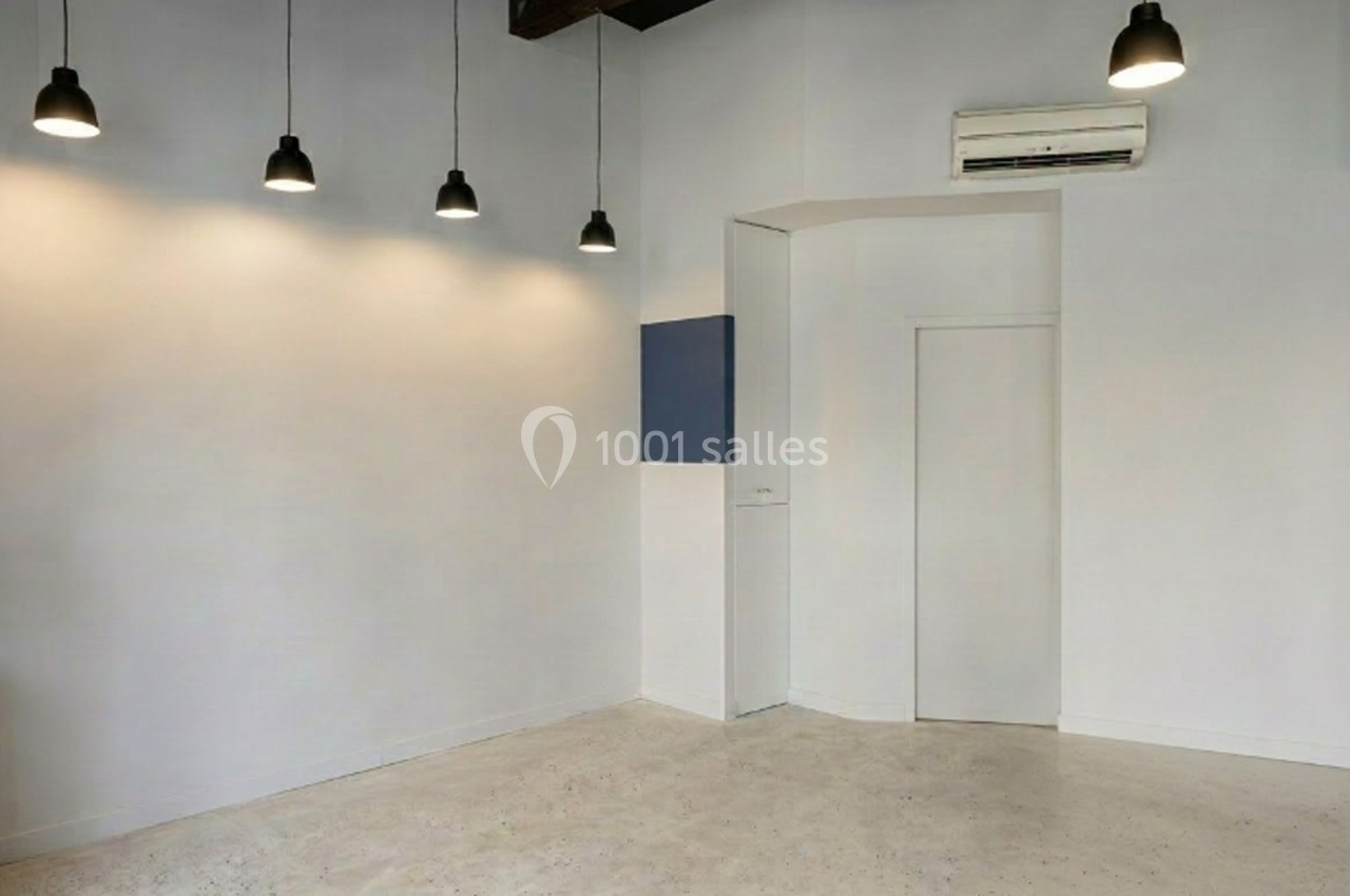 Salle vide avec murs blancs, sol clair, éclairage suspendu et climatisation murale.