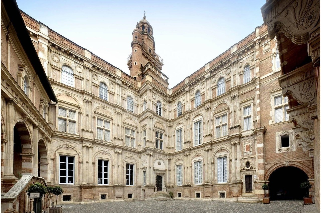 Cour intérieure d'un bâtiment historique en briques et pierre, avec une tour centrale et des fenêtres ornées.
