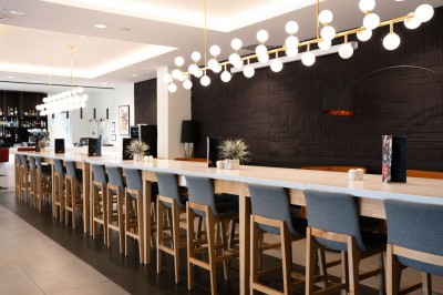 Chambre d'hôtel avec deux lits simples, un fauteuil, un bureau, une lampe et une grande fenêtre avec rideaux.