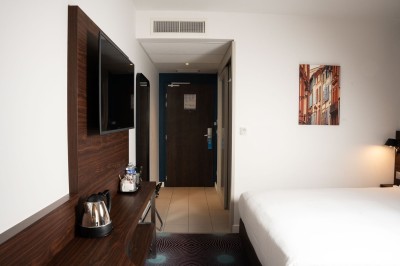 Chambre d'hôtel avec deux lits simples, un fauteuil, un bureau, une lampe et une grande fenêtre avec rideaux.