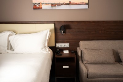 Chambre d'hôtel avec deux lits simples, un fauteuil, un bureau, une lampe et une grande fenêtre avec rideaux.