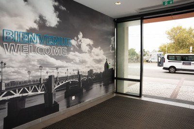 Chambre d'hôtel avec deux lits simples, un fauteuil, un bureau, une lampe et une grande fenêtre avec rideaux.