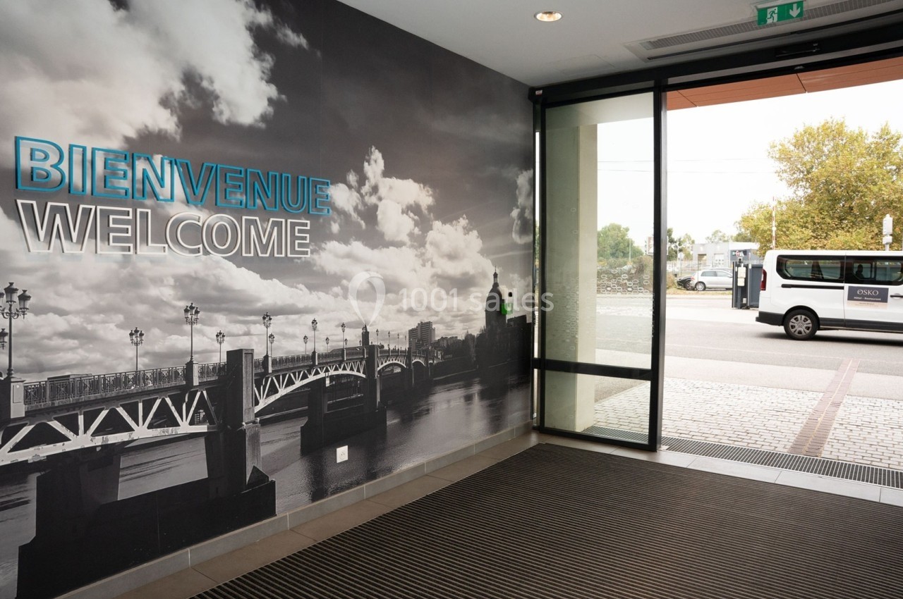 Entrée d'un bâtiment avec un mur décoré d'une photo urbaine et une porte vitrée donnant sur un bus stationné.