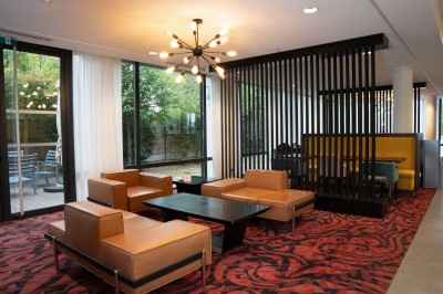 Chambre d'hôtel avec deux lits simples, un fauteuil, un bureau, une lampe et une grande fenêtre avec rideaux.