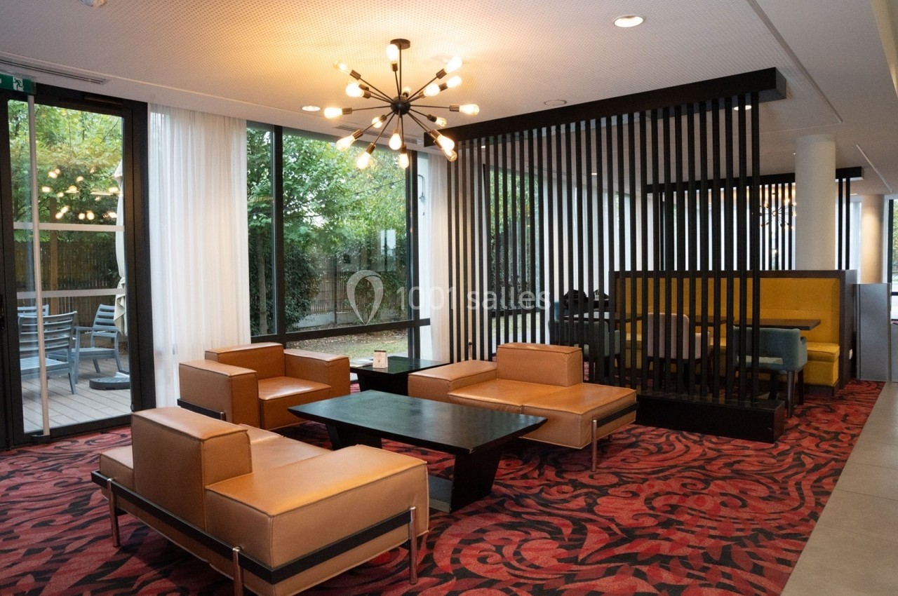 Salon moderne avec fauteuils en cuir, table basse, éclairage design et vue sur une terrasse extérieure arborée.