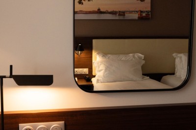 Chambre d'hôtel avec deux lits simples, un fauteuil, un bureau, une lampe et une grande fenêtre avec rideaux.