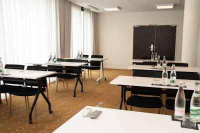Miniature Location salle Blagnac (Haute-Garonne) - Osko #4 Chambre d'hôtel avec deux lits simples, un fauteuil, un bureau, une lampe et une grande fenêtre avec rideaux.